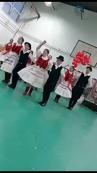 A gyerekcsoport tagjai viseletben, felemelt kézzel a próbateremben